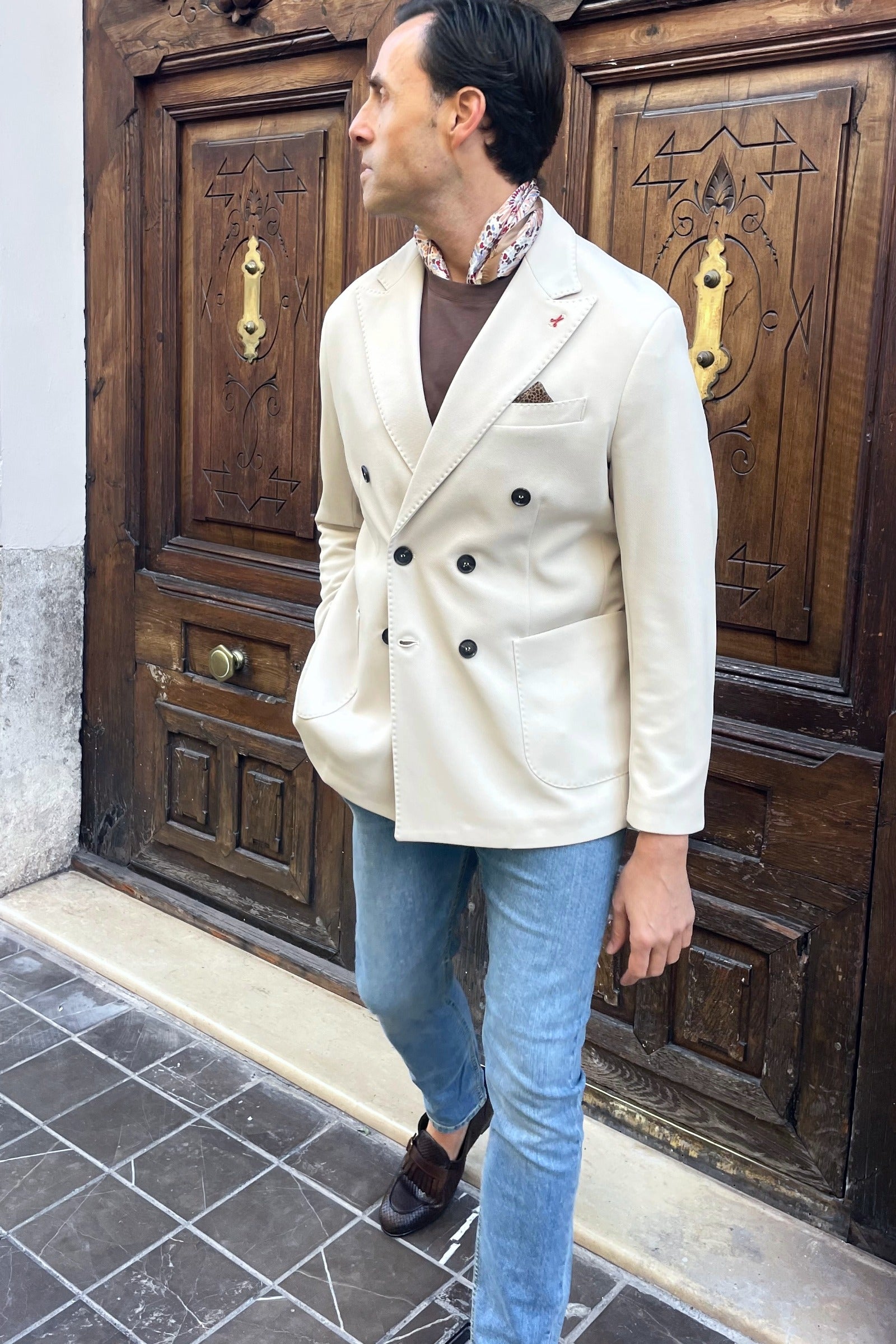 Outfit de hombre con americana cruzada beige combinada con pantalón vaquero y complementos marrones
