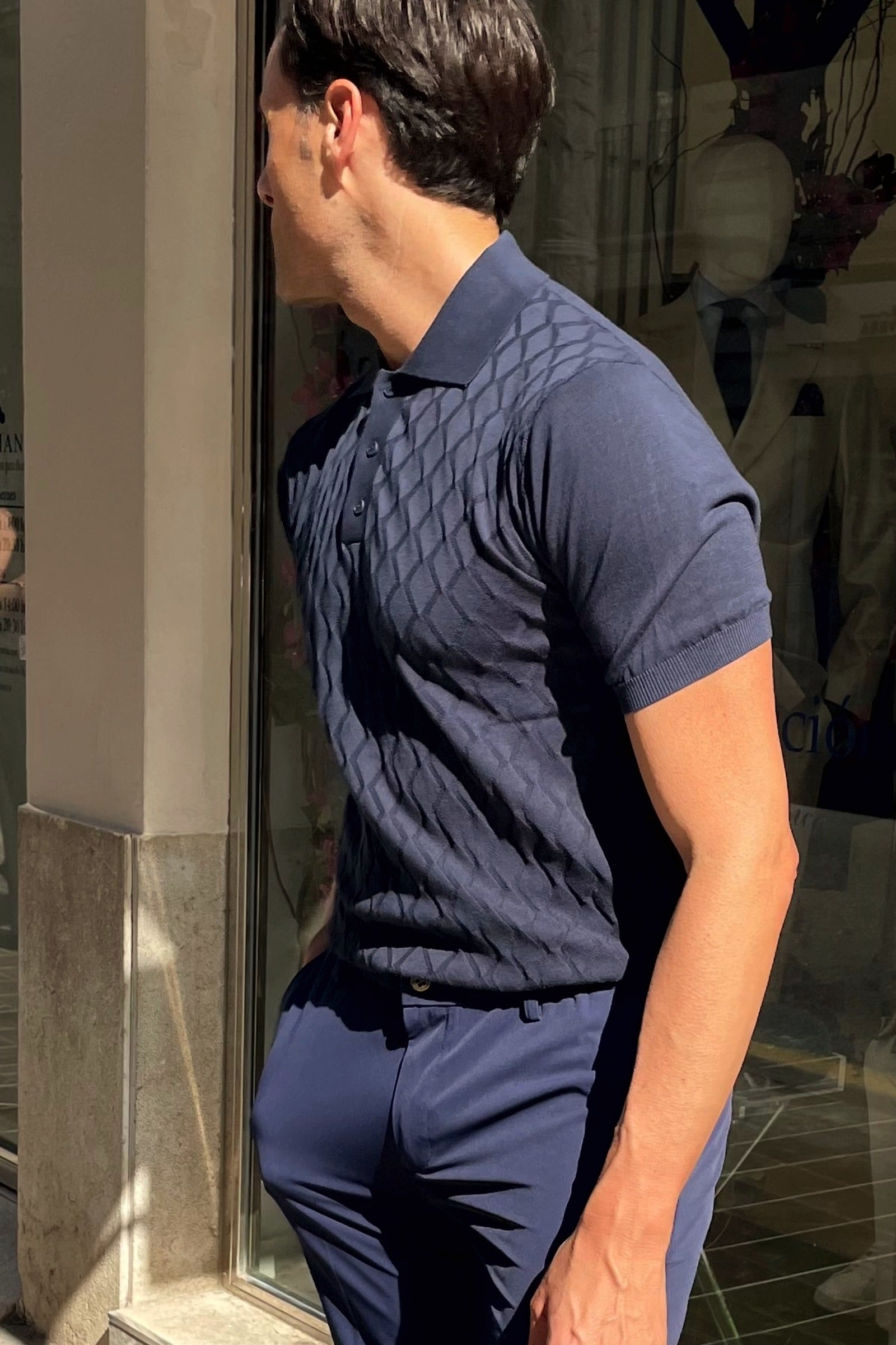 Vista lateral del polo azul marino para hombre con rombos en relieve.